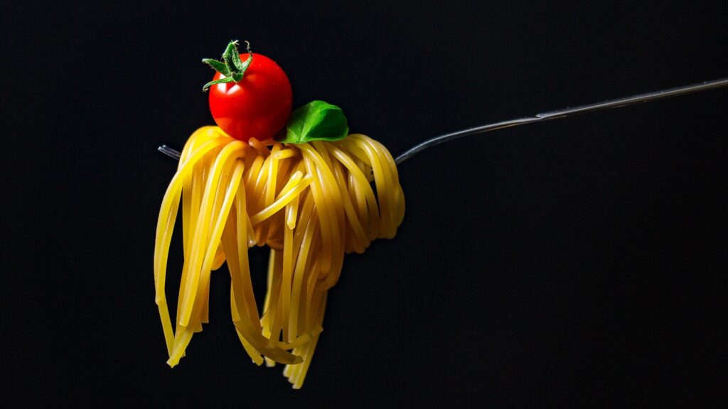 garfo com macarrão, um tomate cereja e uma folha de manjeiricão